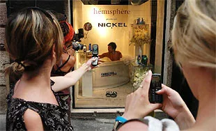 JM Public shower spectators Two women use mobile phones to record a man bathing in a small storefront spa tub labeled