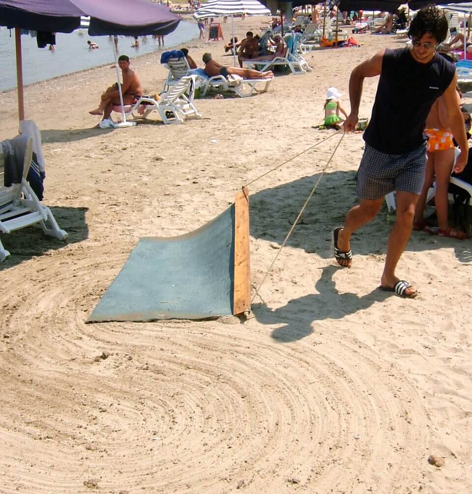 A man sweeping a sandy beach with a tennis rug