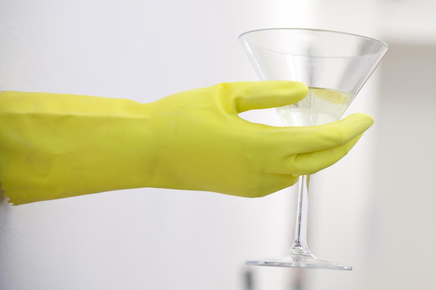 A hand, wearing a yellow rubber glove, is holding a Martini coktail
